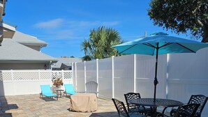 A patio with a table and chairs, a covered umbrella, and a white fence.
