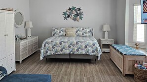 A bedroom with a bed, a dresser, a nightstand, a chair, a ceiling fan, and a window with blinds.