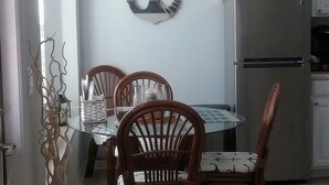 A dining area with a glass-top table, wooden chairs, and a decorative anchor on the wall.