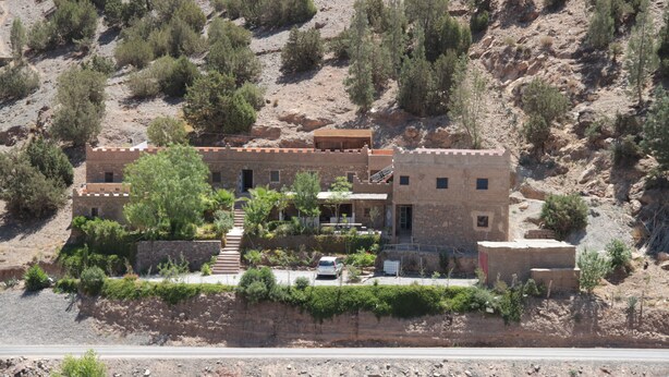 A two-story building with a flat roof, surrounded by sparse vegetation and rocky terrain. - Gite Auberge Tigmmi N Tamazirte (Ijjoukak)