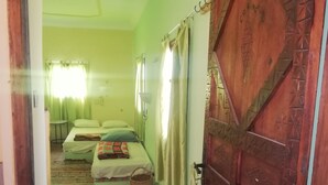 A room with two beds, a wooden door, and a small table with a basket. - Gite Auberge Tigmmi N Tamazirte (Ijjoukak)