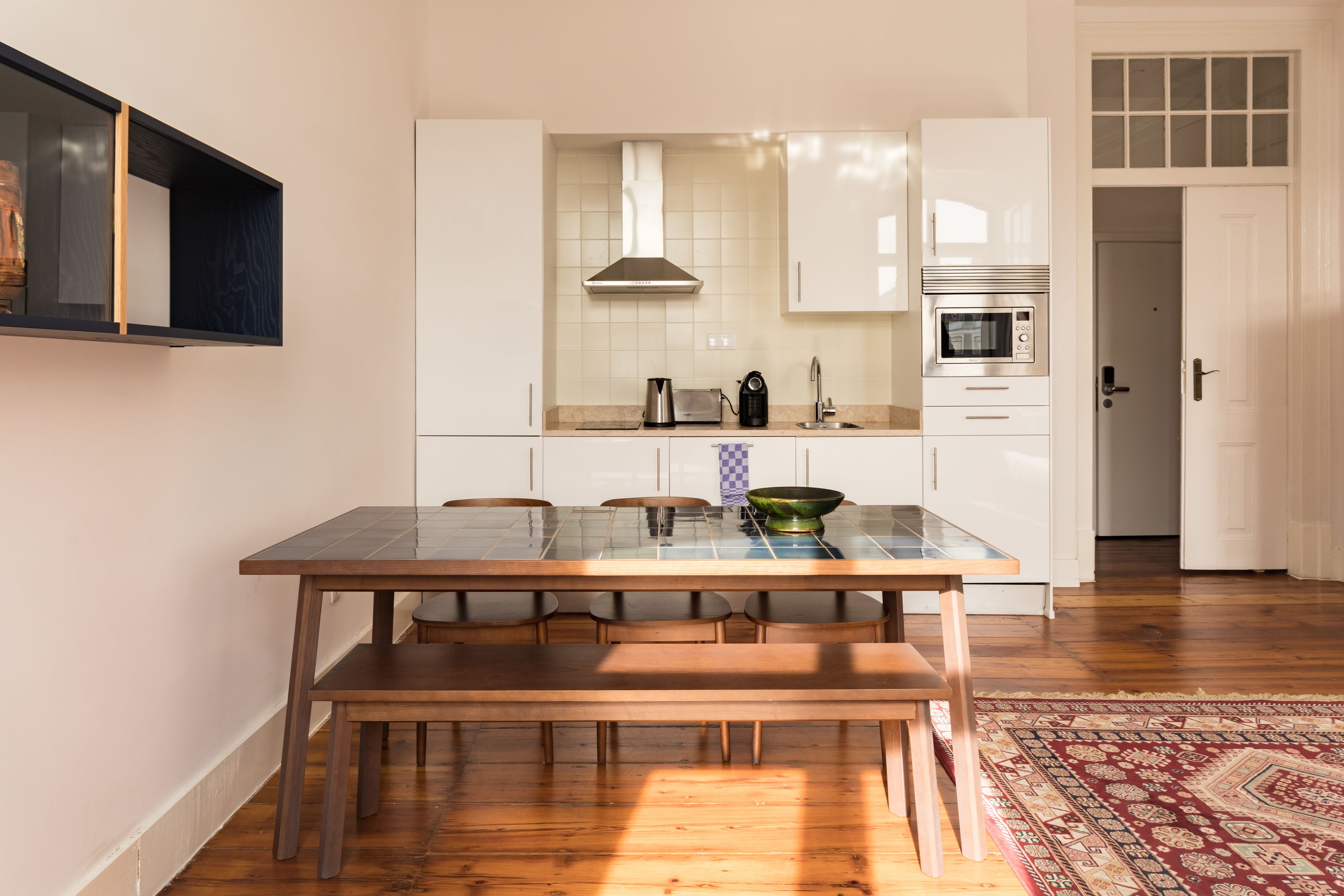 Une cuisine moderne avec des meubles blancs, un four encastré et un coin repas comprenant une table en verre et des chaises en bois.