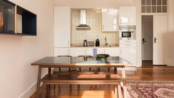 Une cuisine moderne avec des meubles blancs, un four encastré et un coin repas comprenant une table en verre et des chaises en bois.