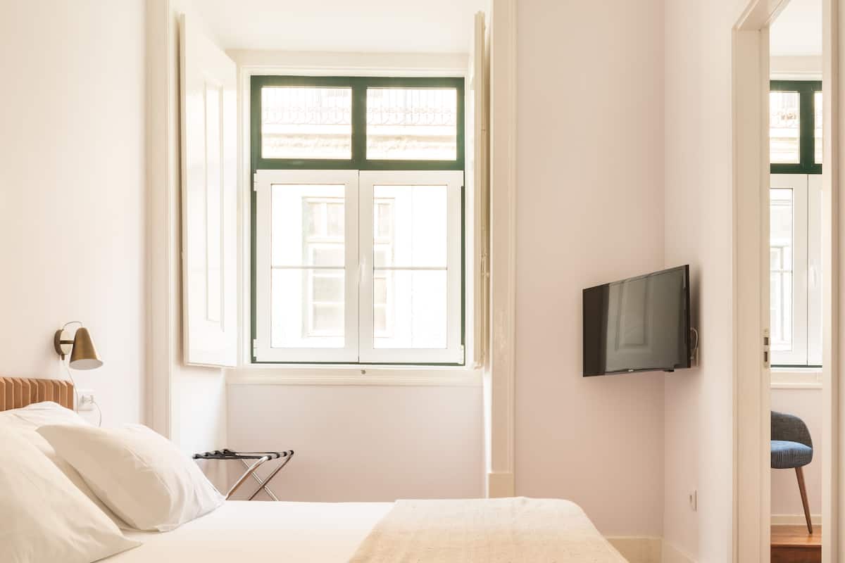Un dormitorio con una cama, un televisor montado en la pared y una ventana con contraventanas verdes.
