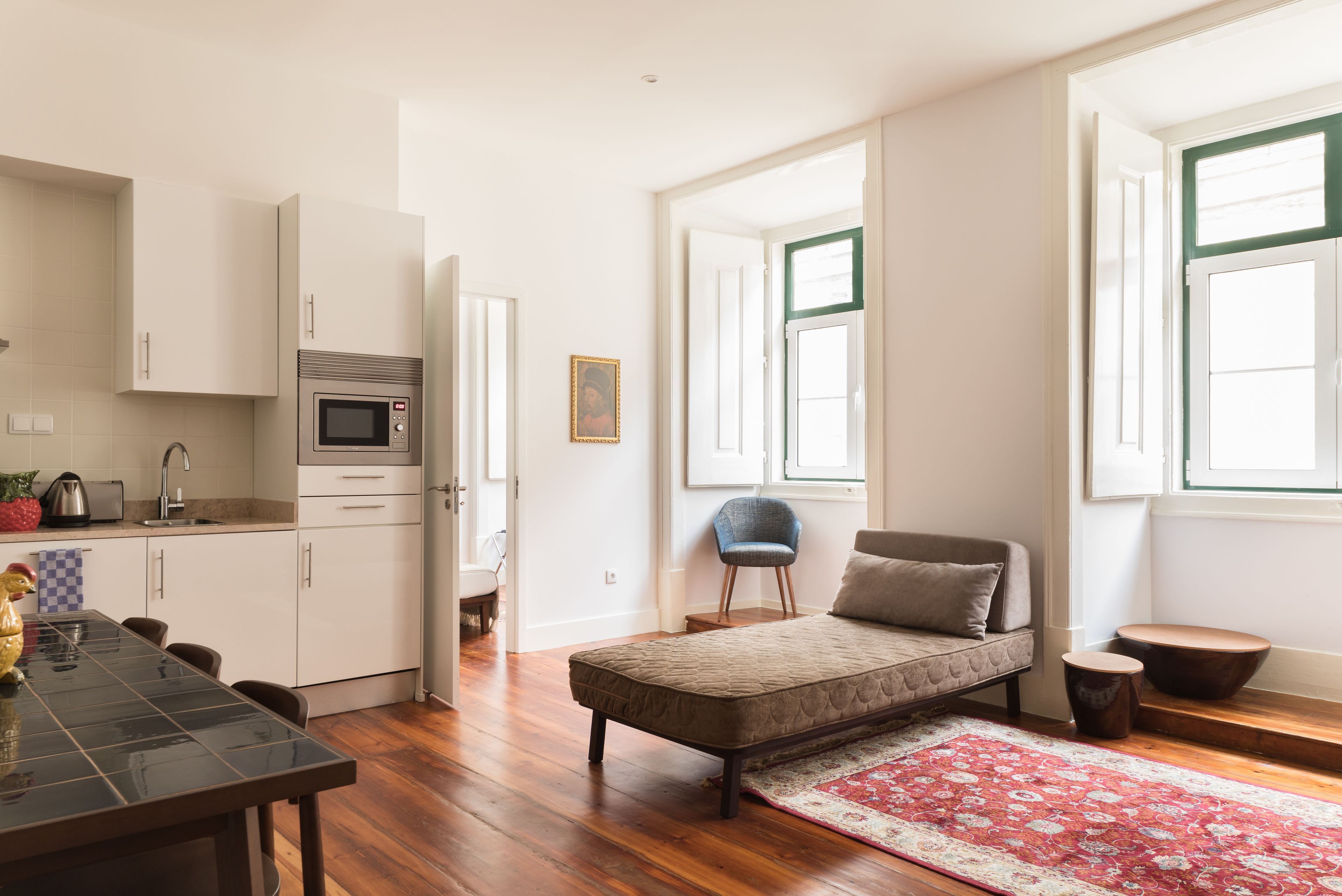A compact living space with a kitchenette, a bed, a dining table, and a large window providing natural light.