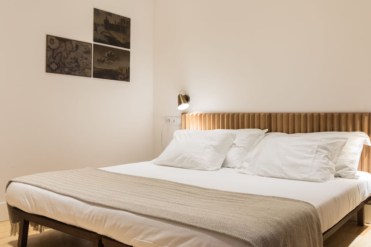 Una cama bien tendida con cabecera de madera, una lámpara de noche y un plaid con estampado de espiga.