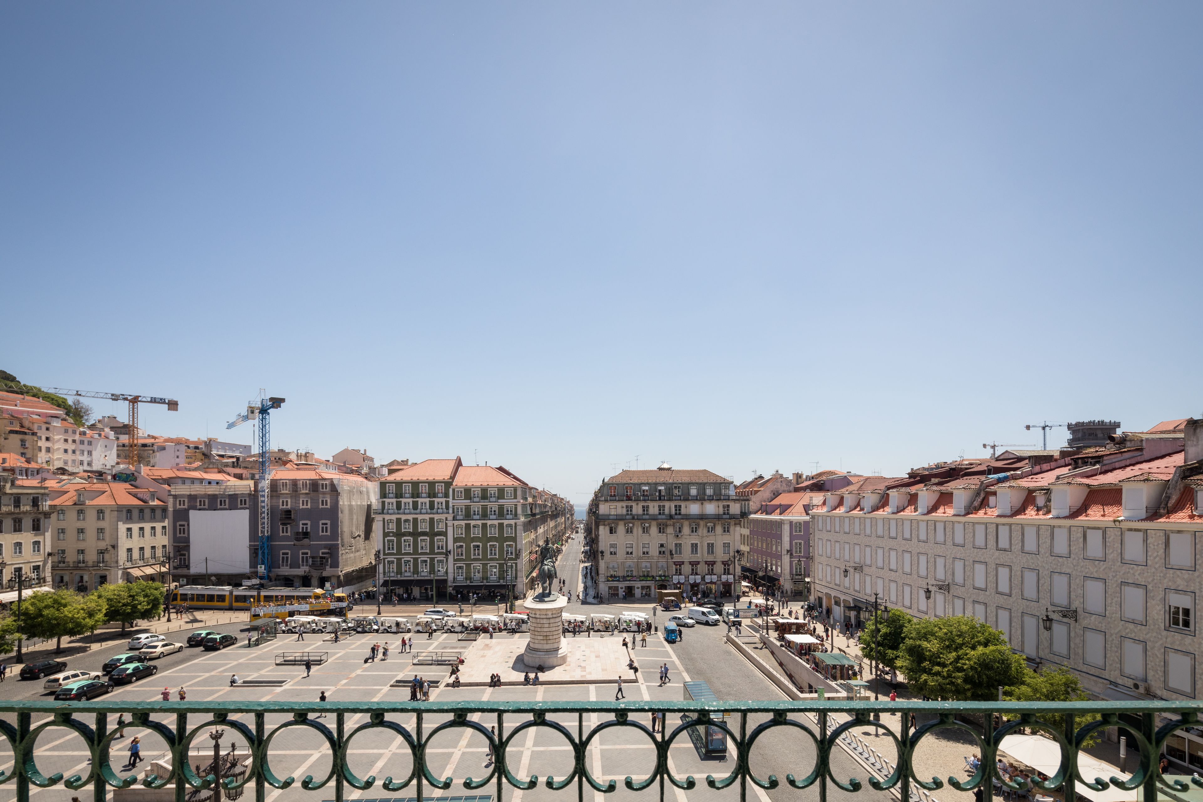 A city square with a central monument, surrounded by historic buildings with red-tiled roofs.