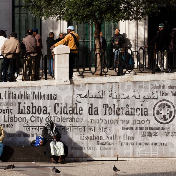 A group of people standing and sitting near a wall with a sign in multiple languages. - The Visionaire Apartments (Lisbon)