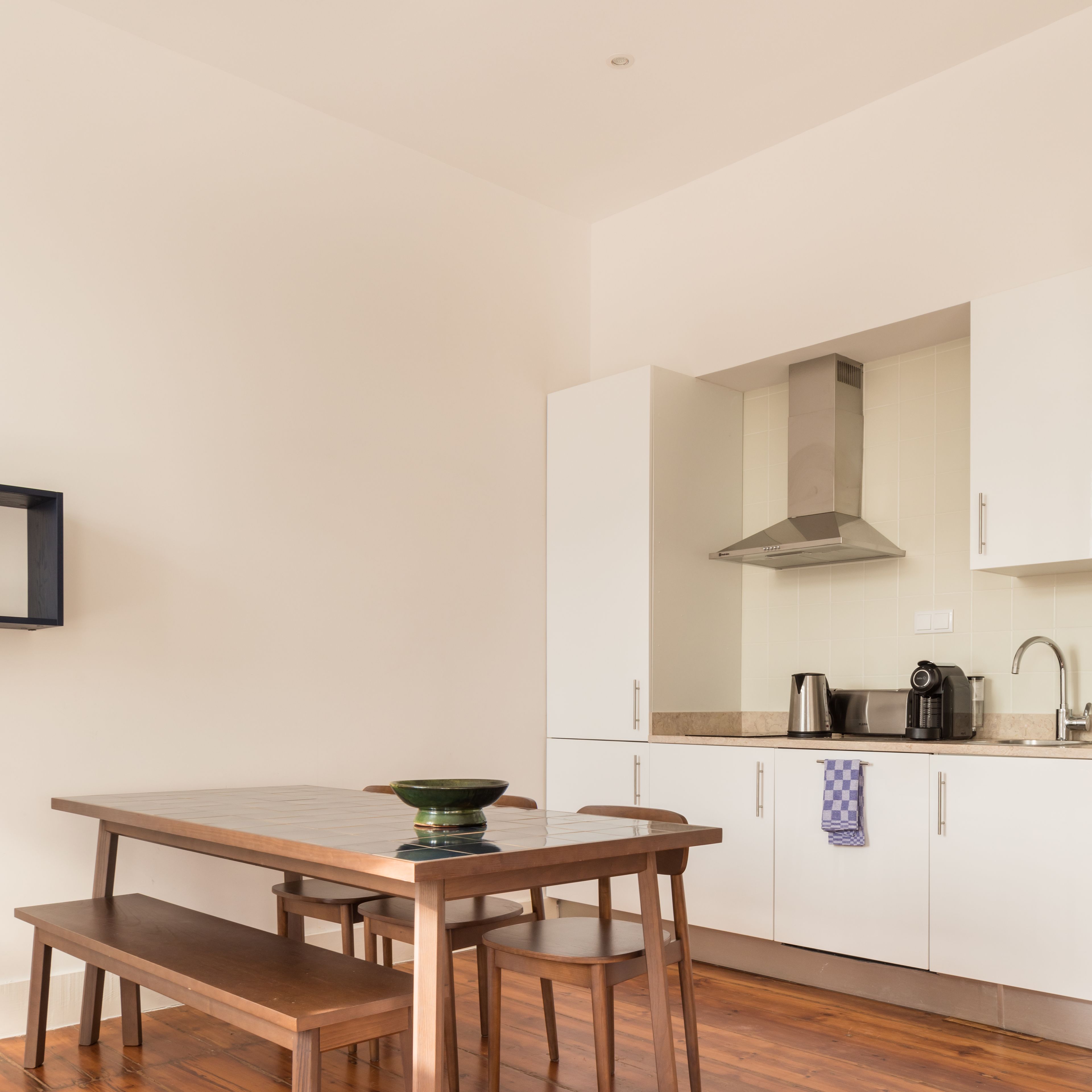 A modern kitchen with white cabinets, a stainless steel range hood, a coffee maker, and a checkered towel hanging on the door.