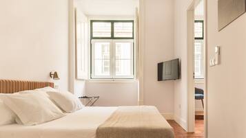 Een slaapkamer met een bed, een televisie, een raam en een deur naar een andere kamer.