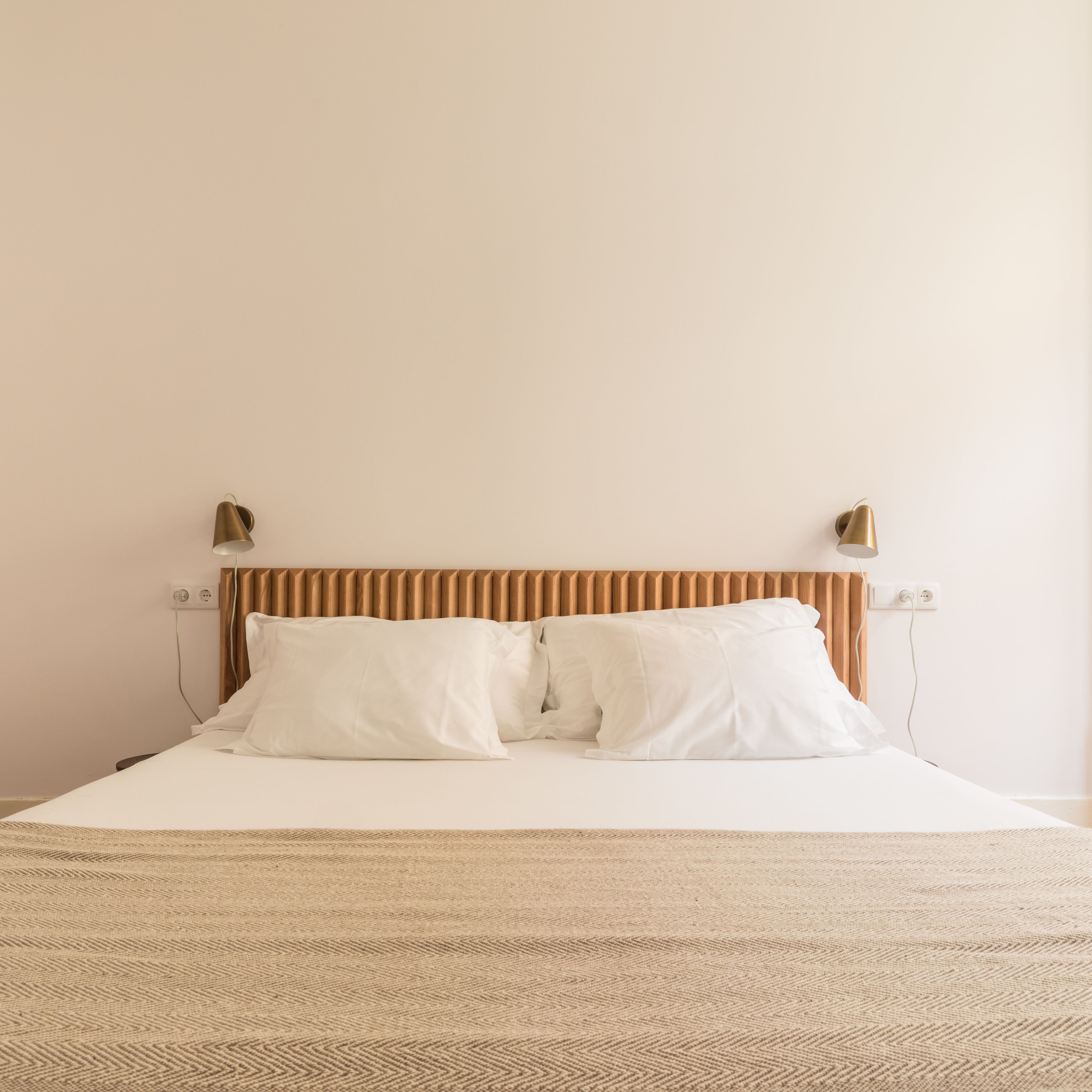 Una cama con cabecera a rayas, dos lámparas de noche y una alfombra estampada.