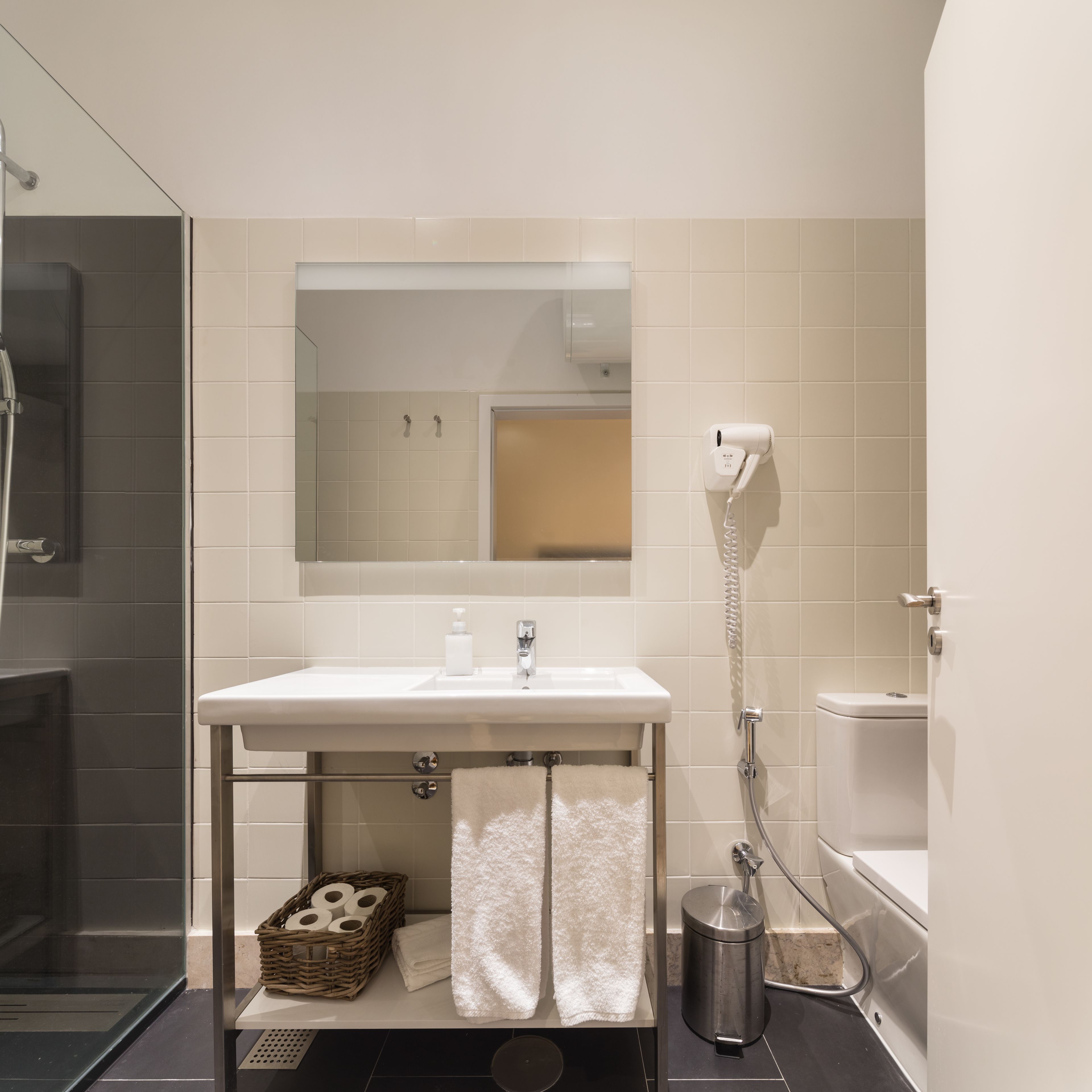 Et moderne badeværelse med en hvid vask, et spejl over vasken, en håndbruser og et toilet.