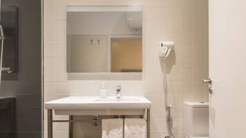 Et moderne badeværelse med en hvid vask, et spejl over vasken, en håndbruser og et toilet.