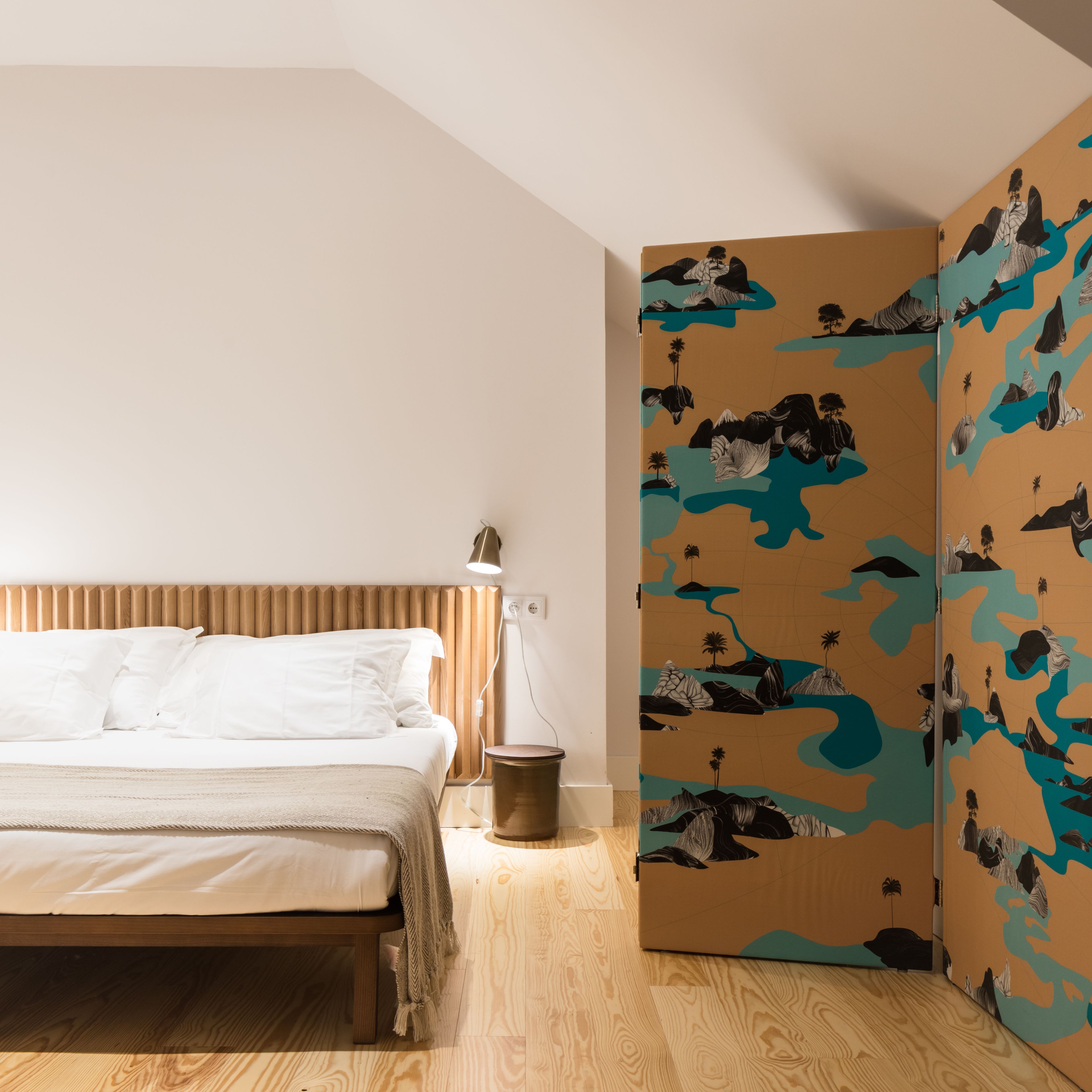 Een slaapkamer met een houten bed, een bedlampje en een kledingkast met een natuurprint.