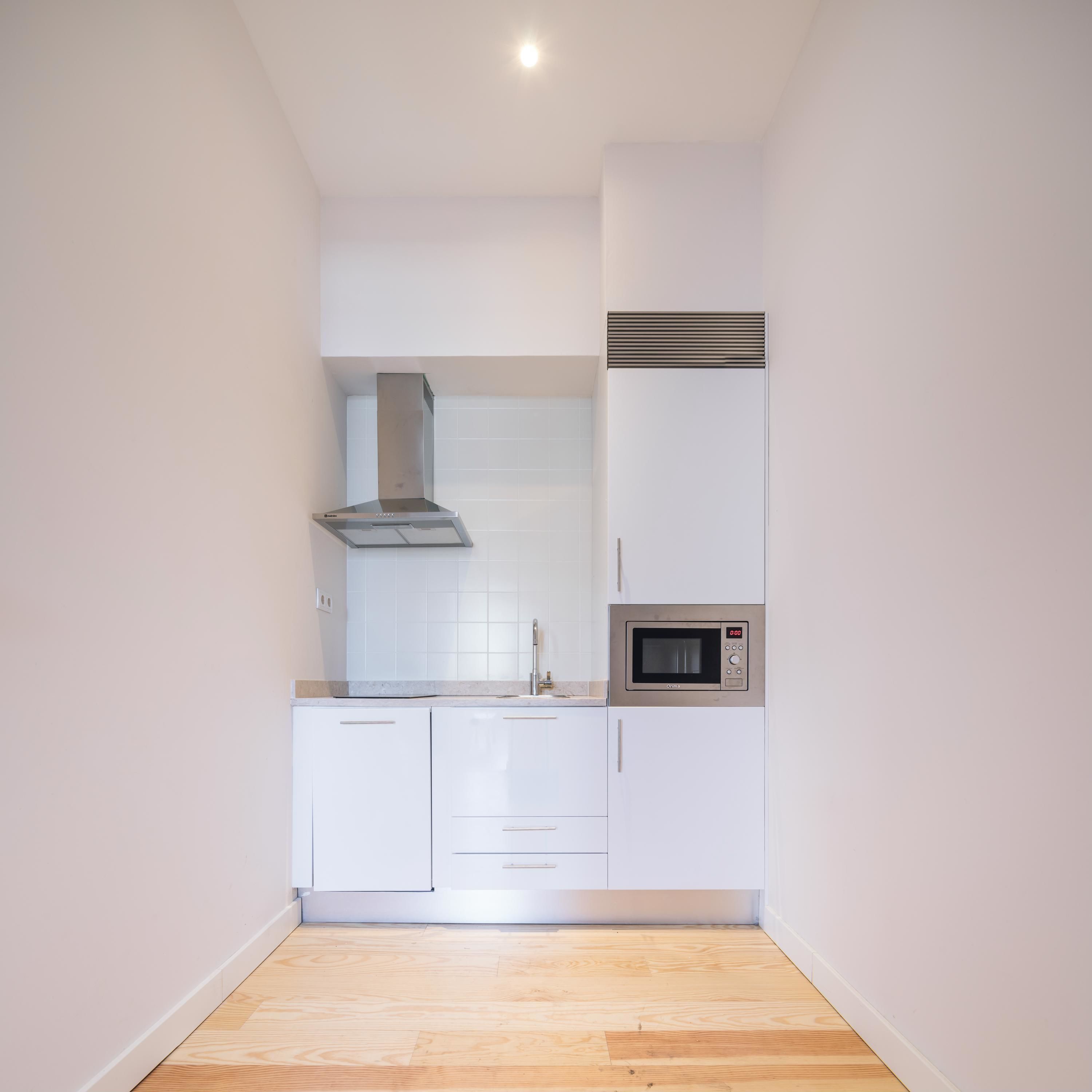 A modern kitchen with white cabinets, a stainless steel range hood, a microwave, and a wooden floor.