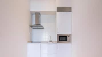 A modern kitchen with white cabinets, a stainless steel range hood, a microwave, and a wooden floor.