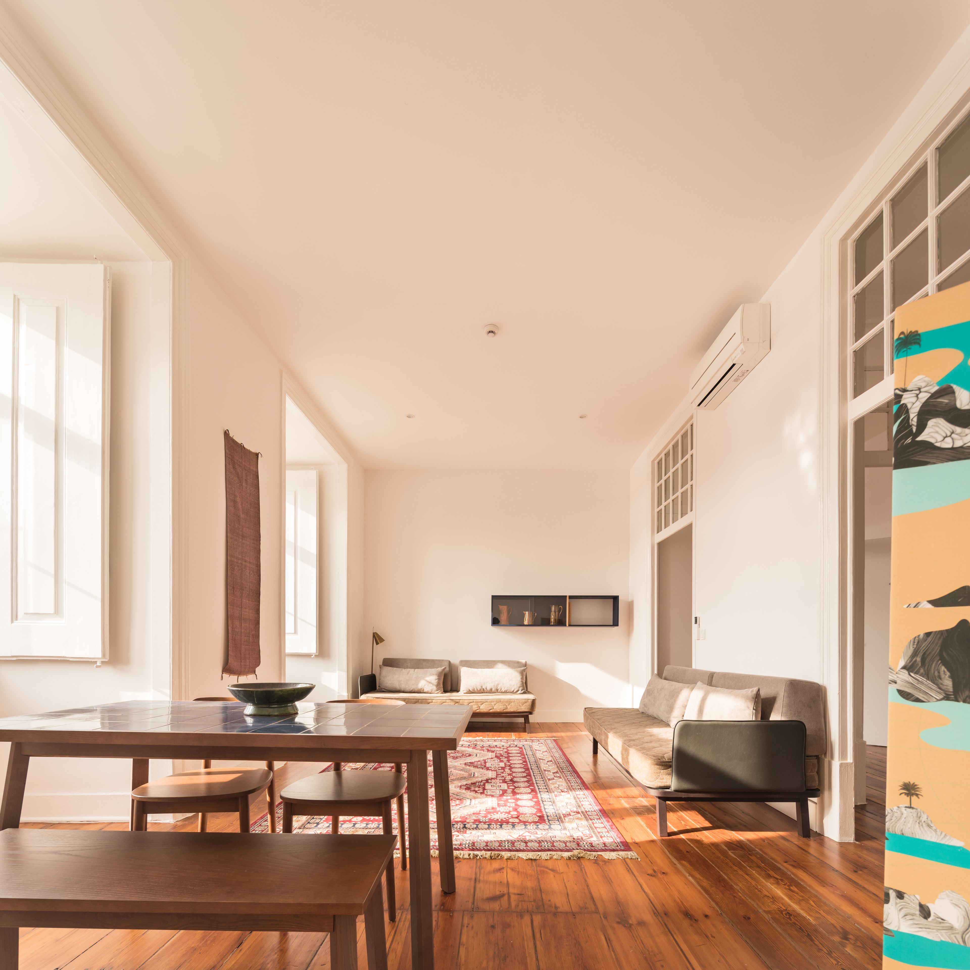 A spacious living area with a wooden floor, a dining table, a sofa, and a TV mounted on the wall.