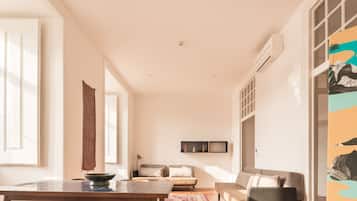 A spacious living area with a wooden floor, a dining table, a sofa, and a TV mounted on the wall.