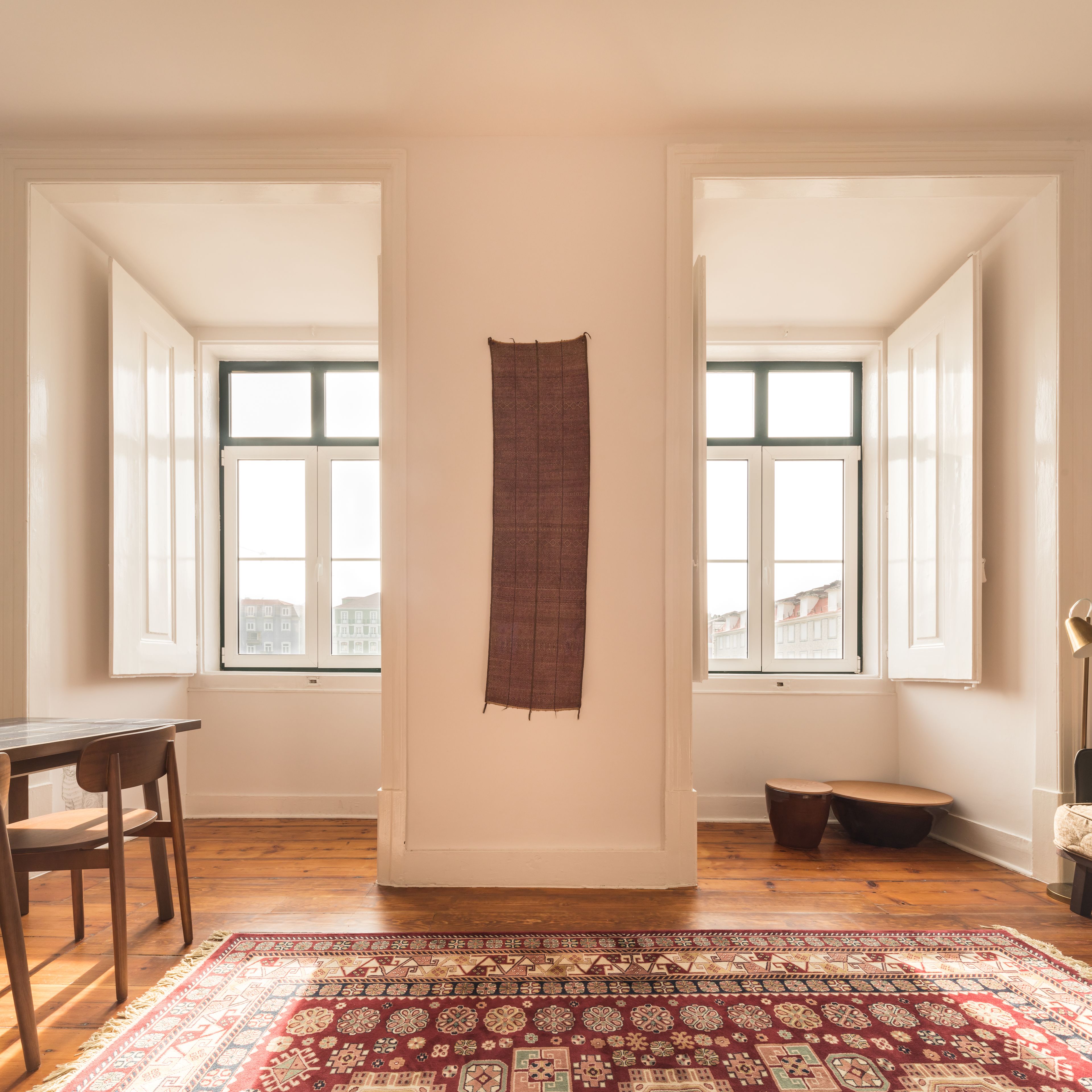 Ein geräumiges Zimmer mit großem Fenster, Holzboden und einem gemusterten Teppich.