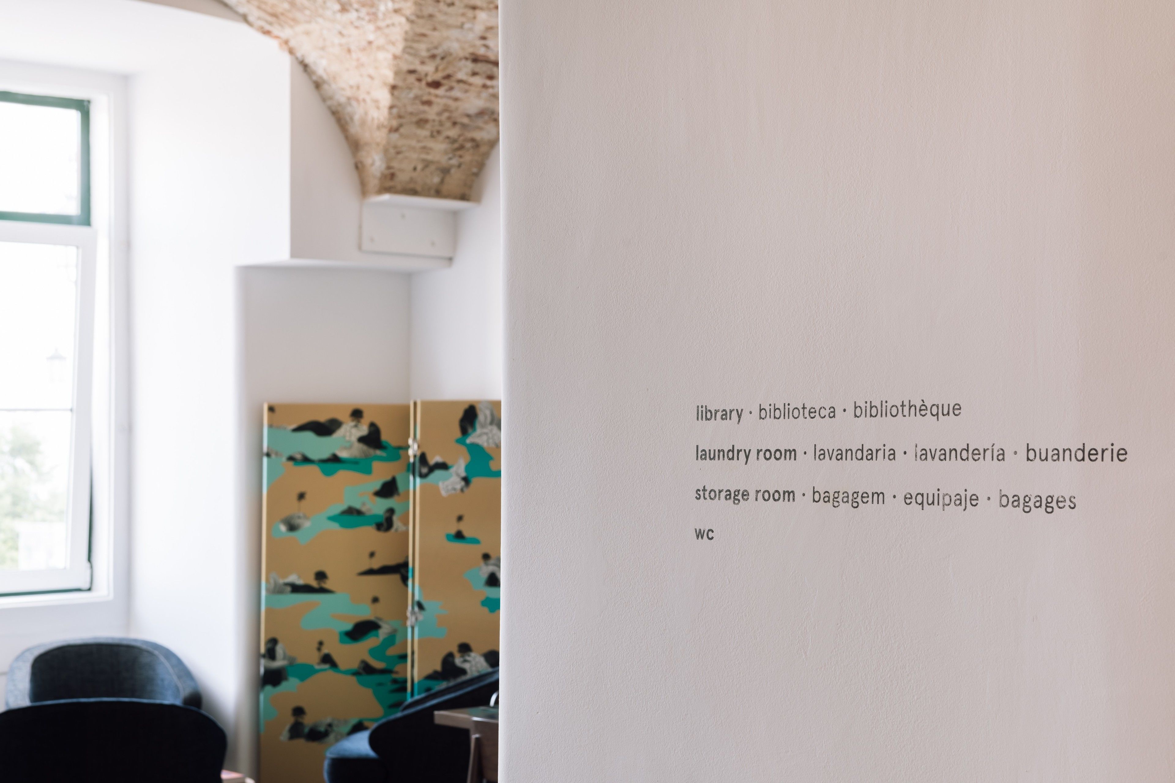 A room with a window, a painting, and a wall with multilingual text listing amenities like a library, laundry room, and storage room.