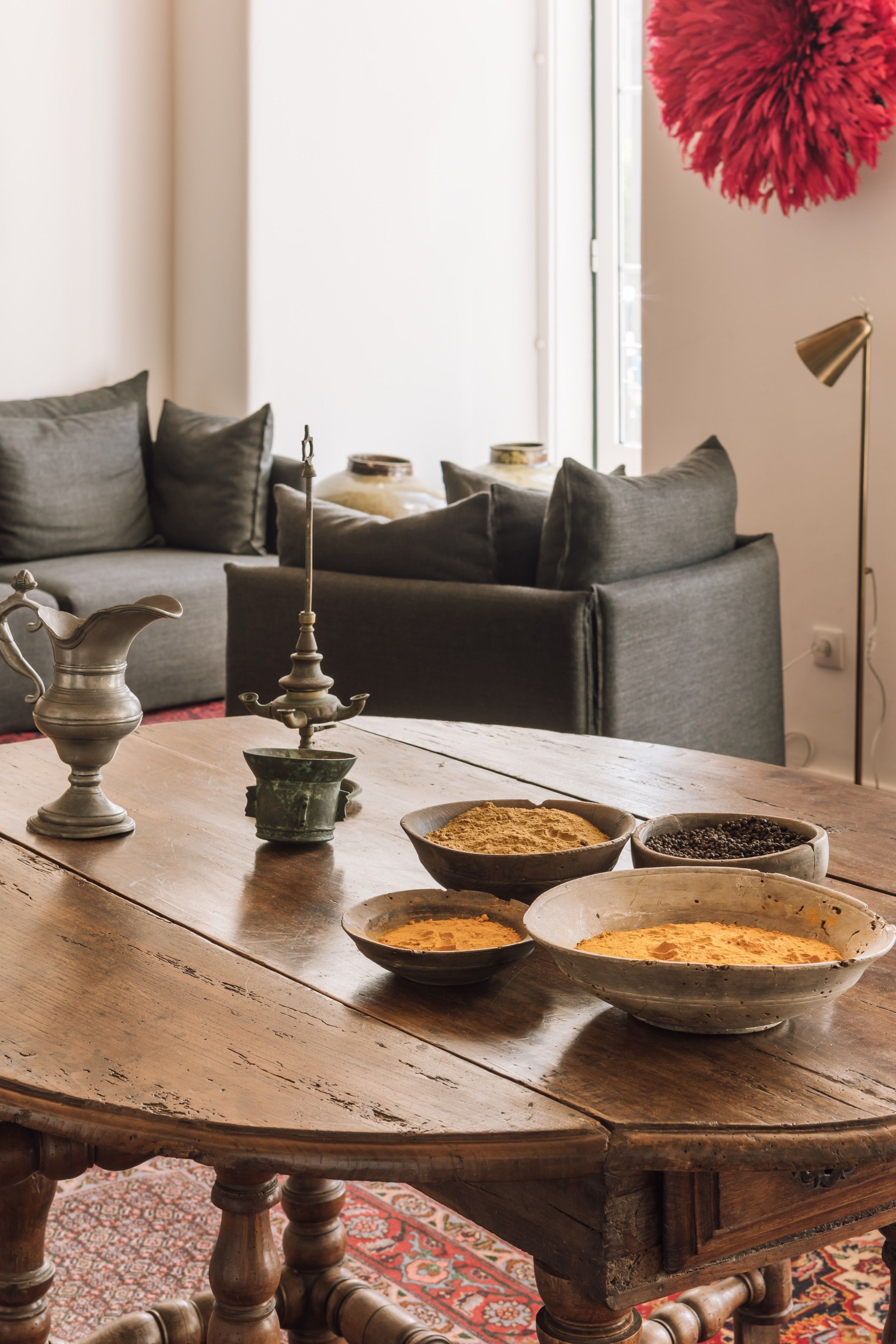 A wooden table with a vintage pitcher, a candle holder, and bowls of spices.