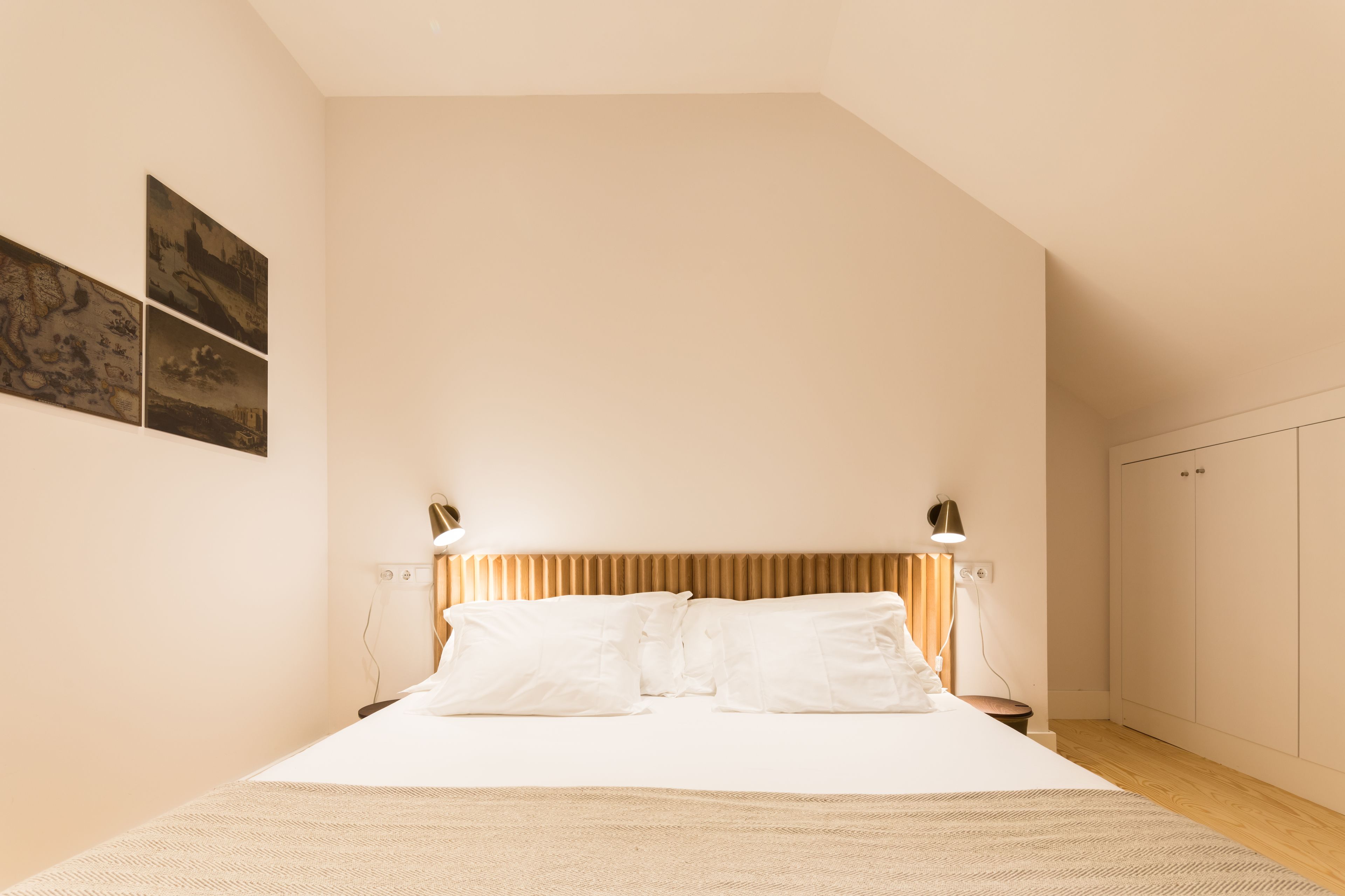 A bedroom with a bed, two bedside lamps, a headboard, and a wardrobe.