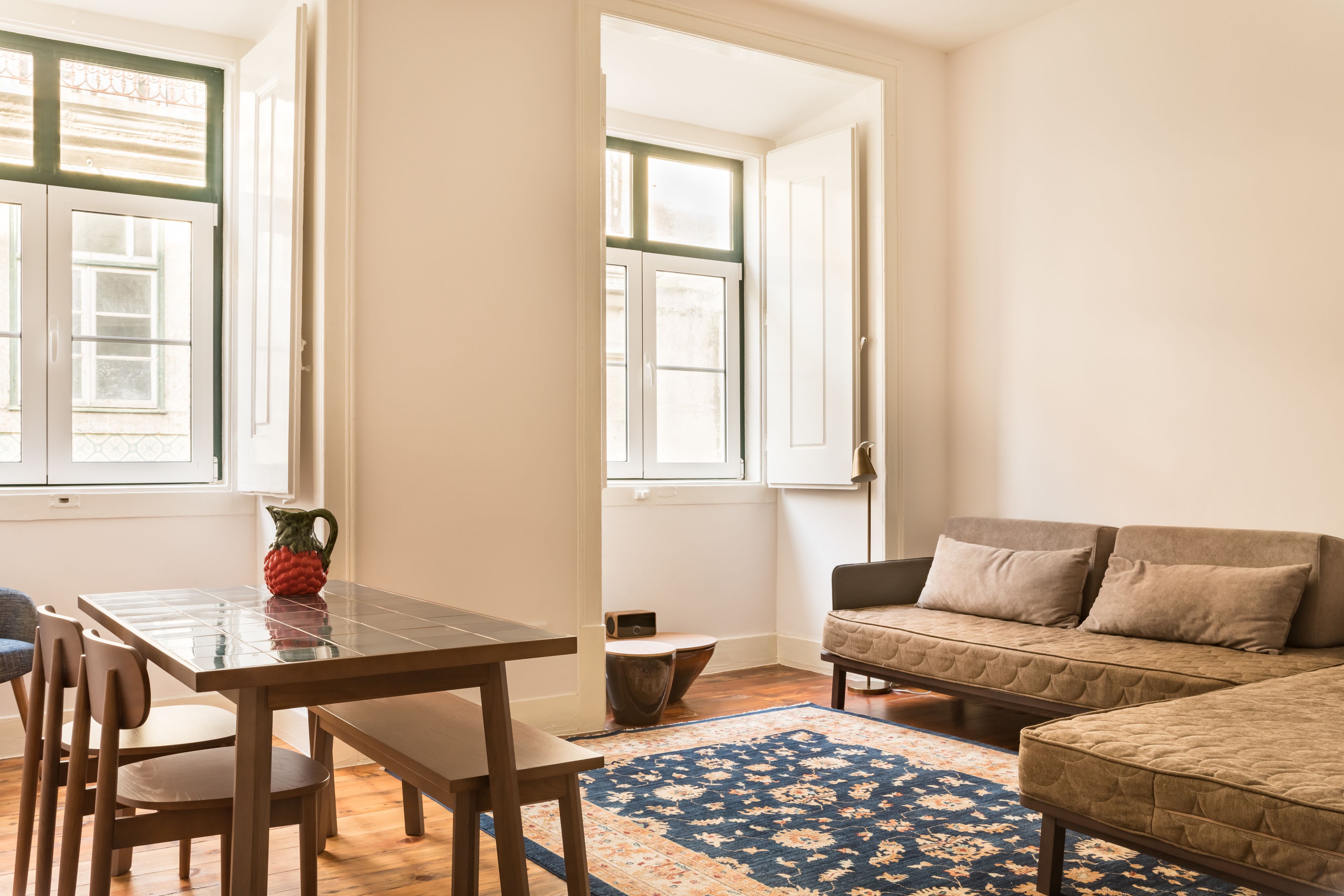 A room with a wooden dining table, chairs, a sofa, and a patterned rug.