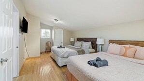 Un dormitorio con dos camas, un televisor montado en la pared y piso de madera.