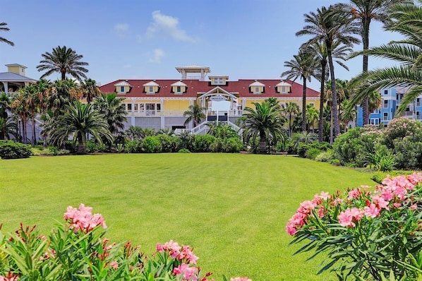Un hotel grande de varios pisos, con una entrada central, rodeado de exuberante vegetación y palmeras.
