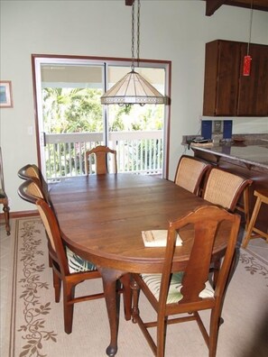 A dining area with a large wooden table and chairs, a hanging light fixture, and a view of a balcony with a white railing.