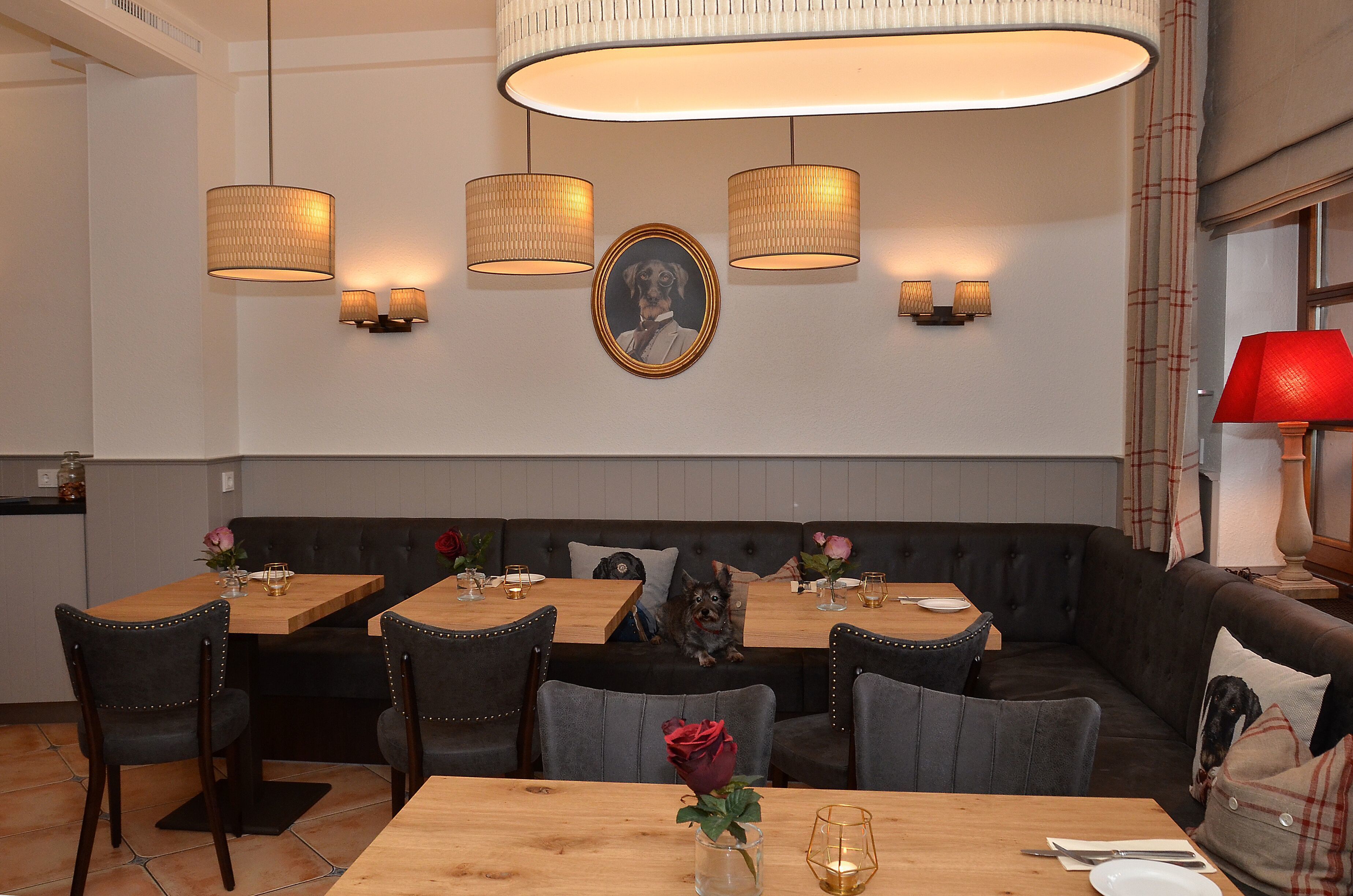 A restaurant with a wooden dining table, black upholstered seating, and pendant lighting.