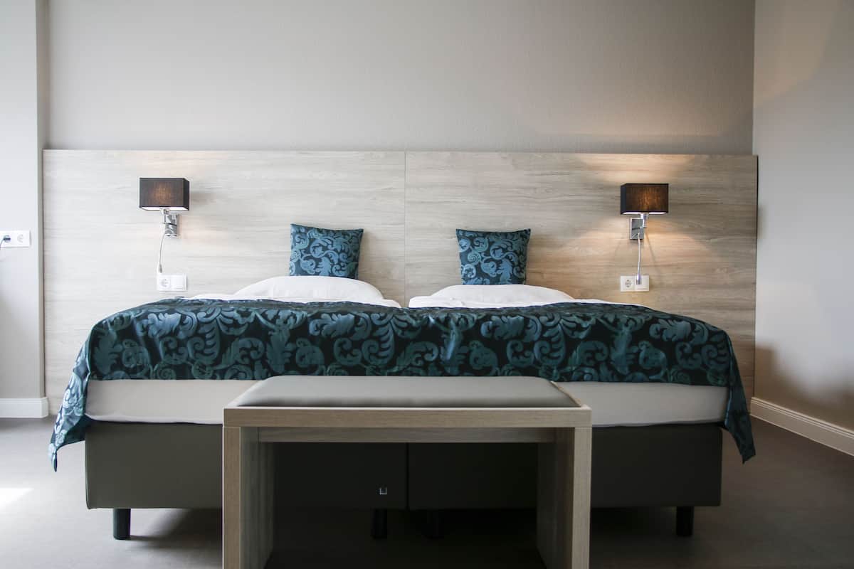 Un lit double avec une couvre-lit à motifs, deux lampes fixées au mur et une table de chevet avec des tiroirs.