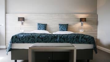 A double bed with a patterned bedspread, two wall-mounted lamps, and a bedside table with drawers.