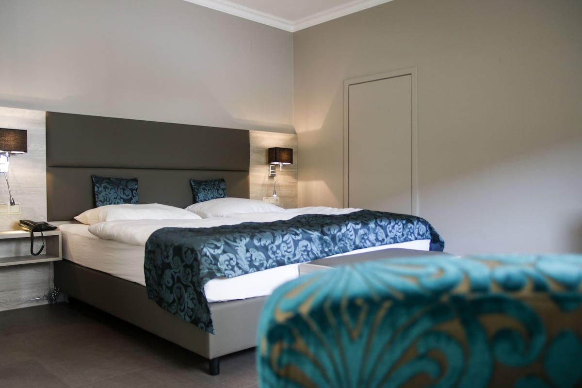Quarto de hotel com cama, luminárias de cabeceira, mesa de cabeceira e uma cadeira.