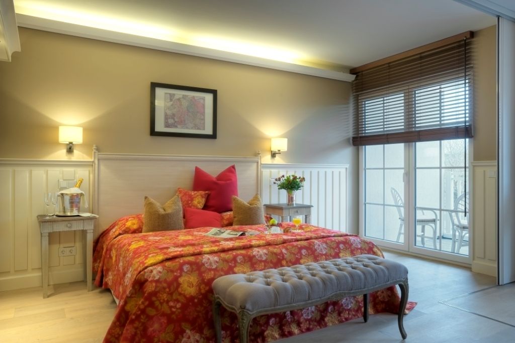 Un dormitorio con una cama grande, dos mesitas de noche, un banco, una ventana con persianas y vistas al exterior.