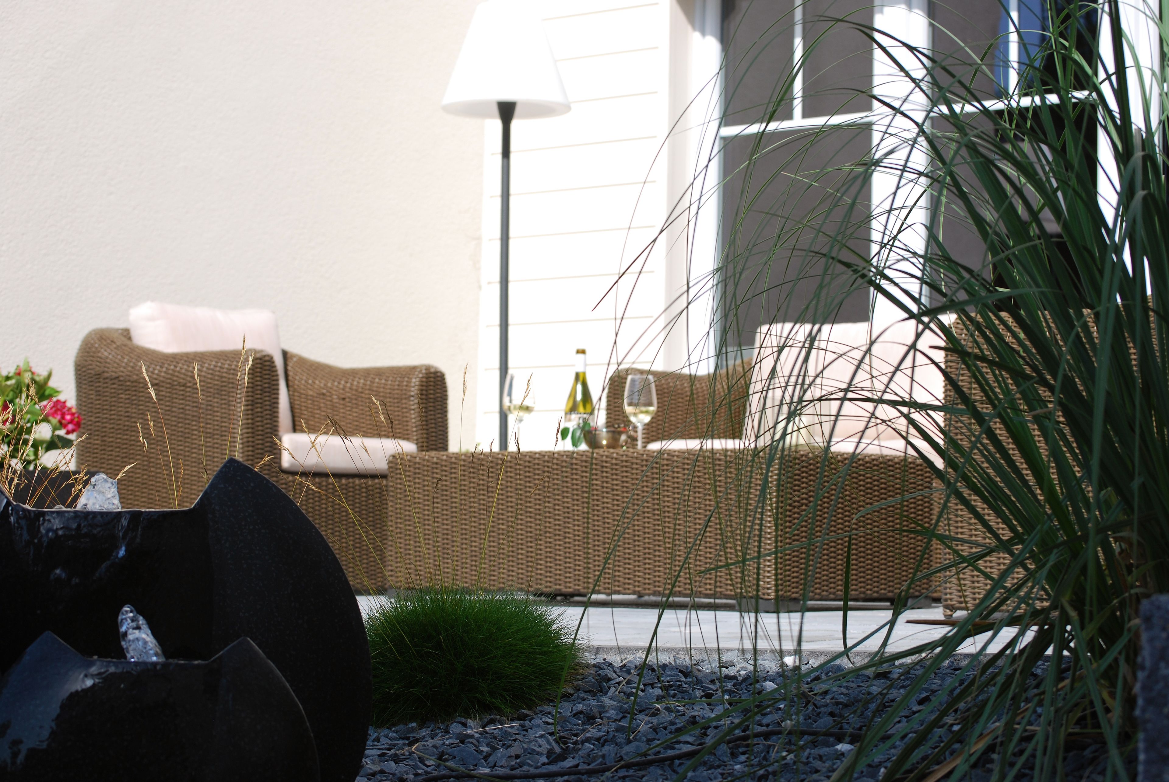 A wicker sofa with cushions, a floor lamp, and a potted plant in a well-lit outdoor seating area.