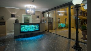 A reception area with a large aquarium, a chandelier, and a glass door leading outside. - Hotel Zur Traube (Perl)
