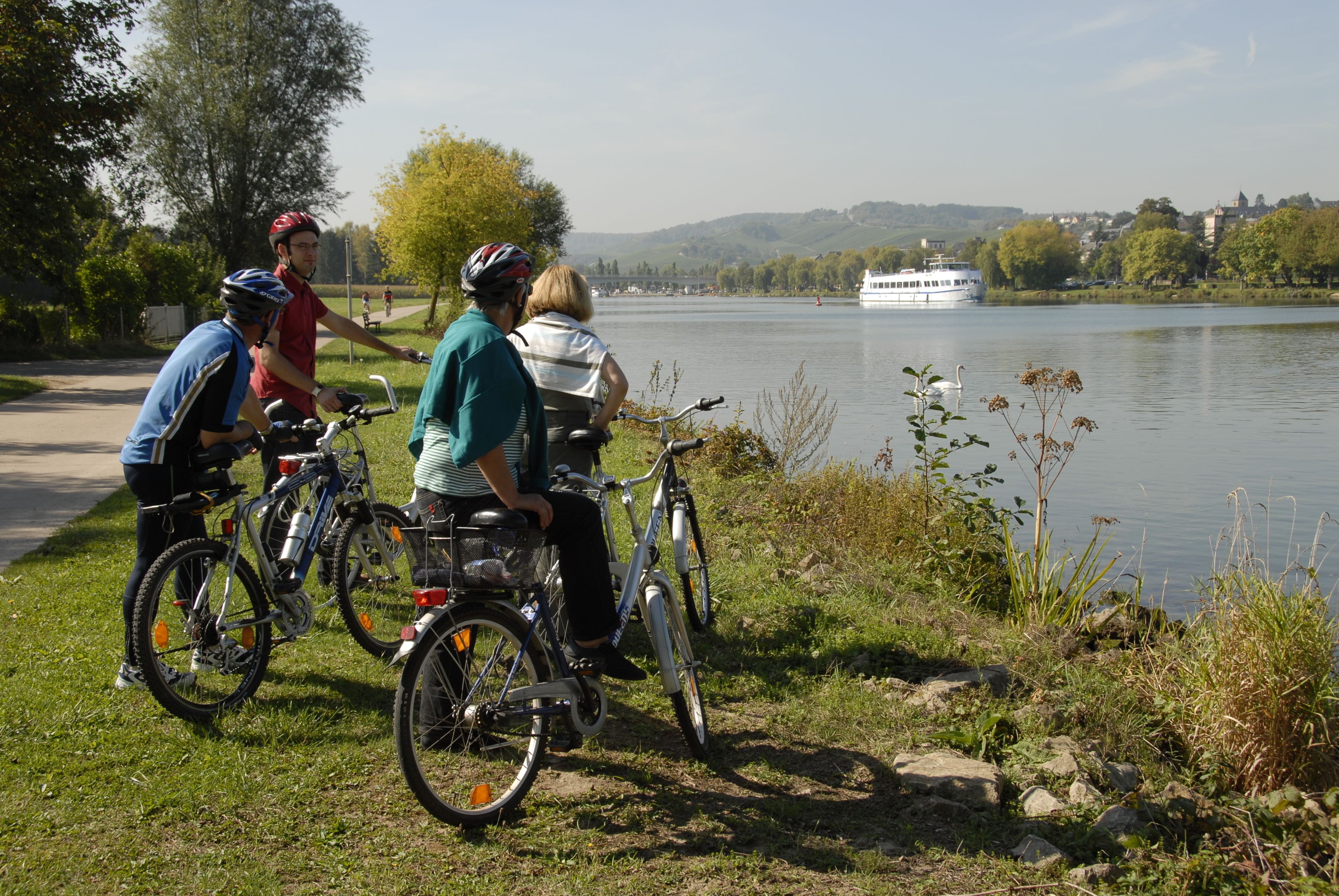 Un grupo de personas en bicicleta junto a un lago, con un bote al fondo.