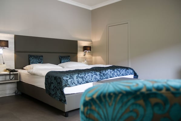 Una habitación de hotel moderna con una cama grande, lámparas de noche, una mesita de noche y una puerta.