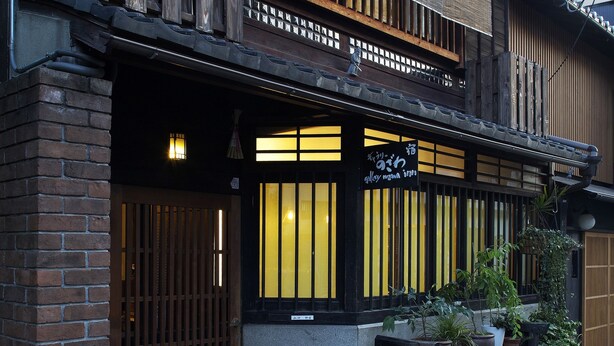 A traditional Japanese building with a wooden facade, a black signboard, and potted plants on the sidewalk. - Gallery Nozawa Inn (Kyoto)