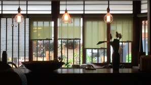 A dimly lit room with large windows, a wooden table, and hanging light fixtures. - Gallery Nozawa Inn (Kyoto)