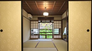 A traditional Japanese room with tatami flooring, sliding doors, and a view of greenery outside. - Gallery Nozawa Inn (Kyoto)
