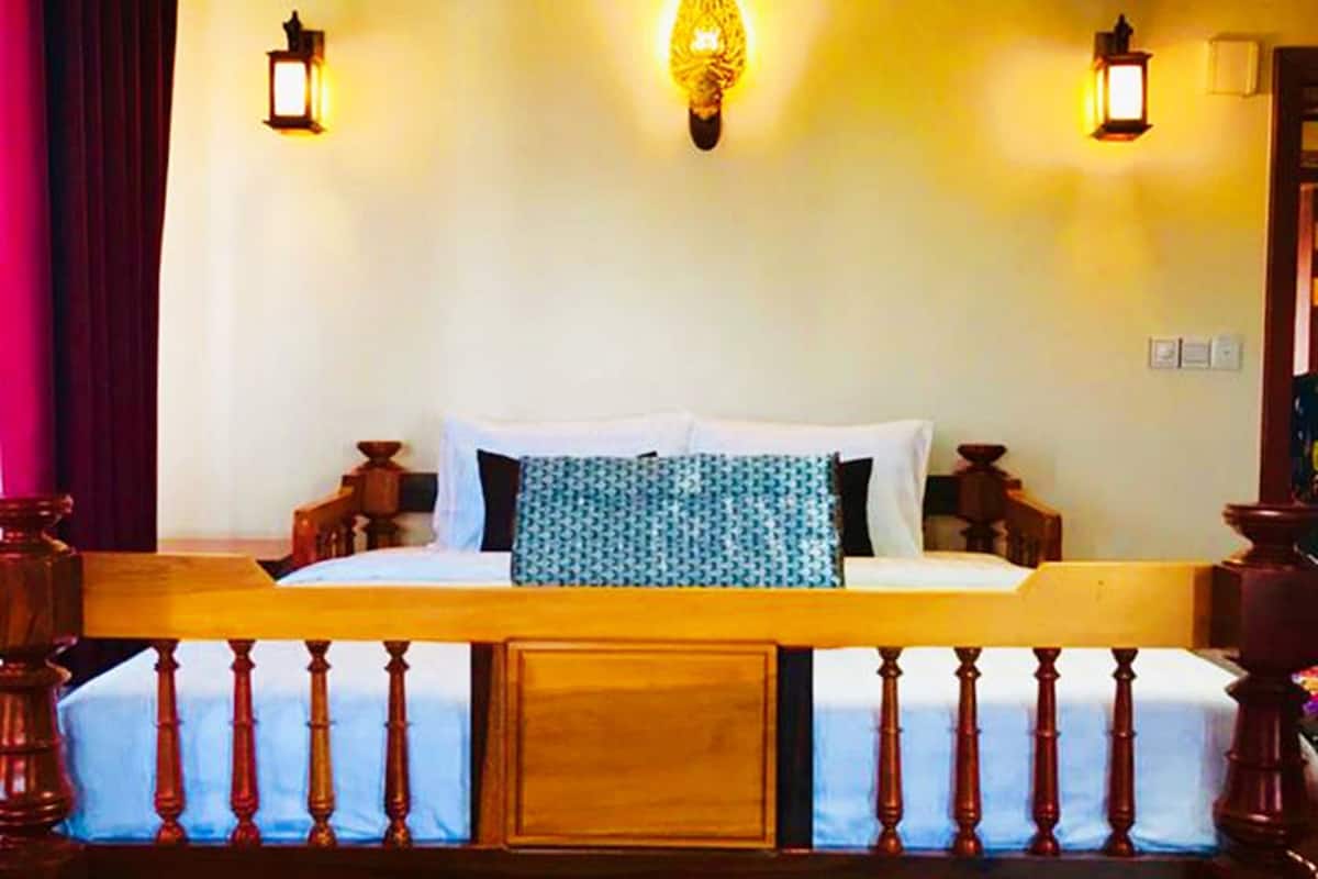 Quarto com cama, cabeceira de madeira, duas luminárias fixadas na parede e um detalhe decorativo verde.