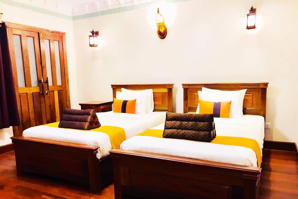 Quarto de hotel com duas camas, cabeceiras de madeira e um guarda-roupa.