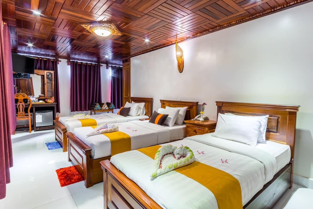 Quarto de hotel com quatro camas, cabeceiras de madeira, um espelho, uma escrivaninha com um computador e um tapete vermelho.