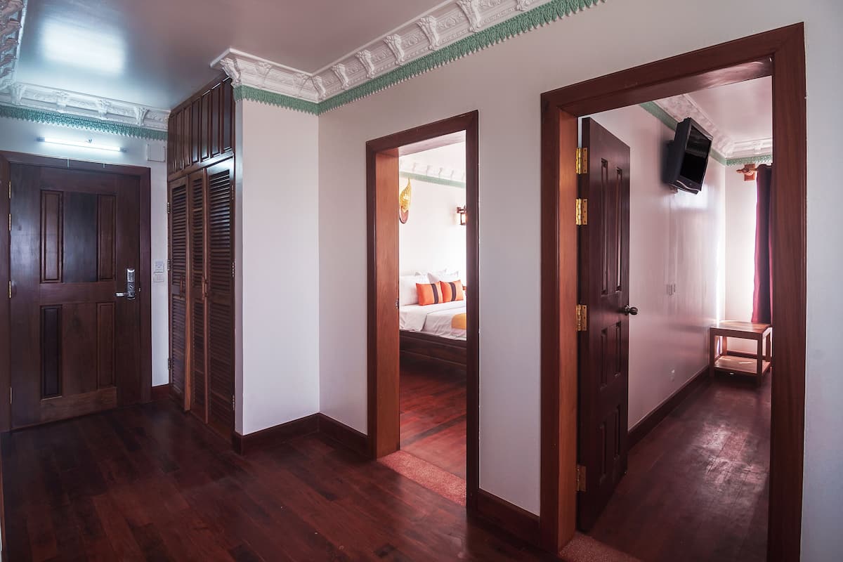 Corredor com portas de madeira e uma cama visível através de uma porta aberta.