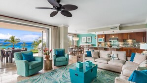 A spacious living area with a view of the ocean, a kitchen with wooden cabinets, and a dining area with a table and chairs. - Maui Resort Rentals: Honua Kai Konea 351, 3BR w/ Direct Oceanfront Views + B.B.Q. on Balcony! (Lahaina)