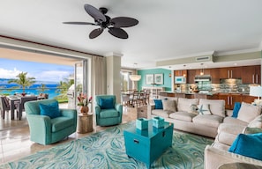 Een ruime woonkamer met turquoise en beige meubels, een keuken met houten kastjes en een balkon met uitzicht op de oceaan.