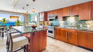 A modern kitchen with wooden cabinets, a large island with bar stools, a stove, oven, and a microwave. - Maui Resort Rentals: Honua Kai Konea 351, 3BR w/ Direct Oceanfront Views + B.B.Q. on Balcony! (Lahaina)
