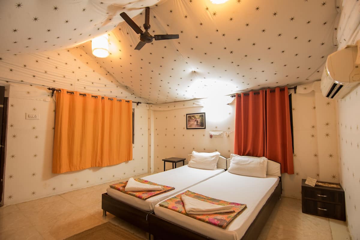 Una habitación de hotel con cama, ventilador de techo, aire acondicionado y ventana con cortinas.